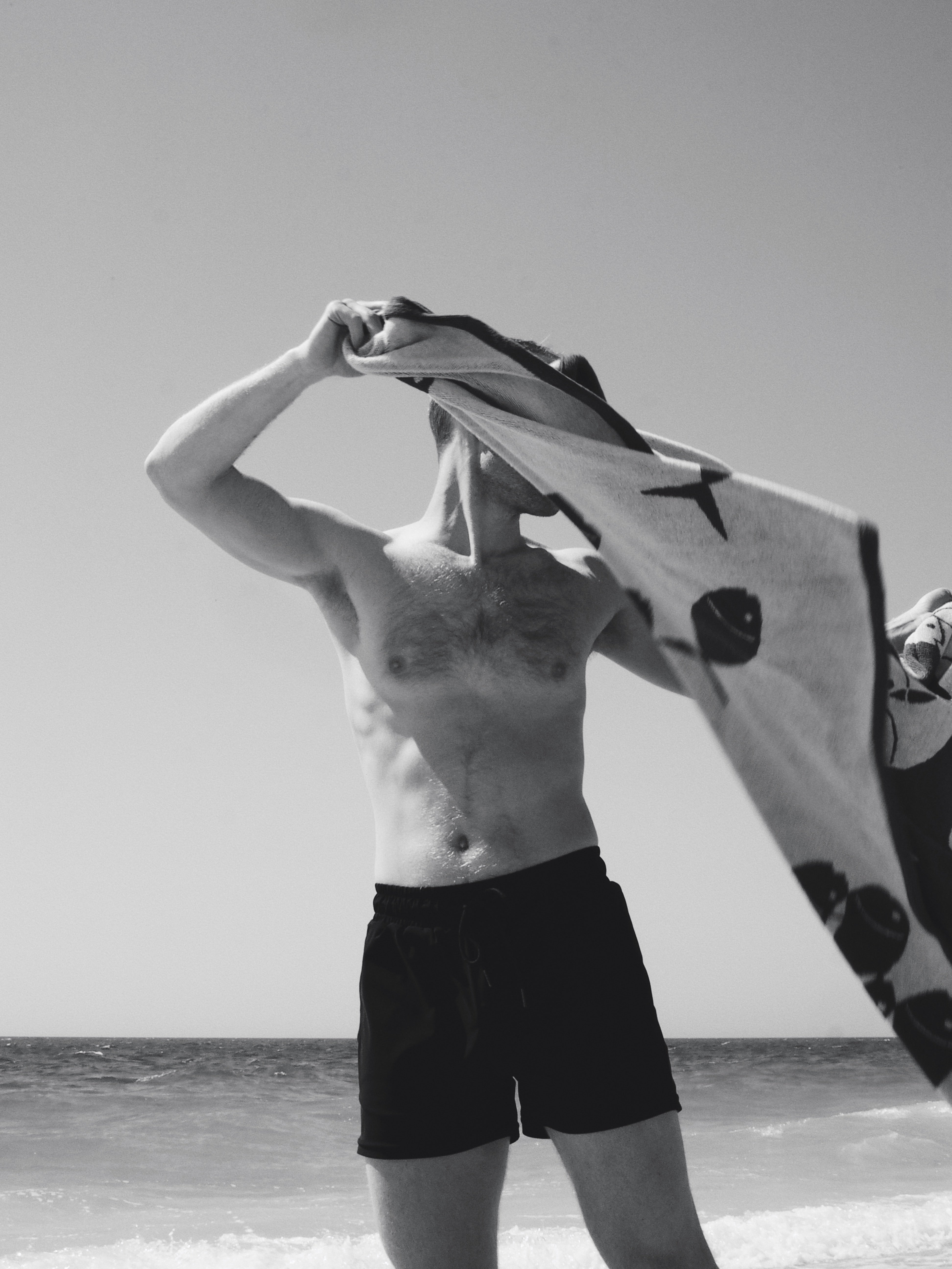 Man wearing black swim trunks holding a towel at the beach