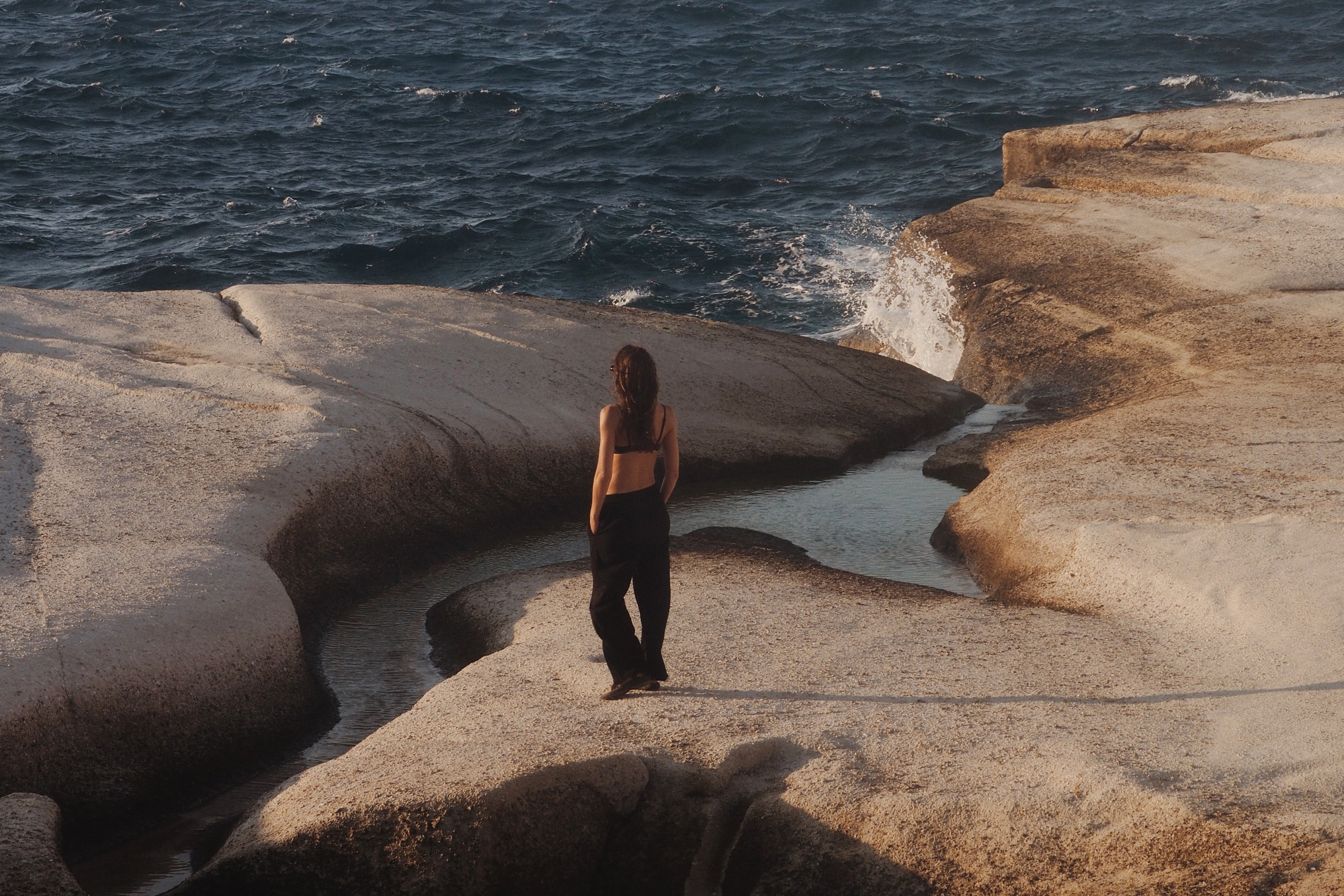 Woman wearing a bikini standing on a rock cliff looking at the ocean with a 'Shop Women's' button.